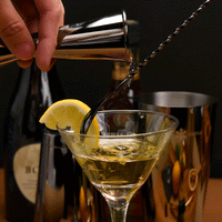 Black Japanese double jigger pouring over bar spoon into martini glass