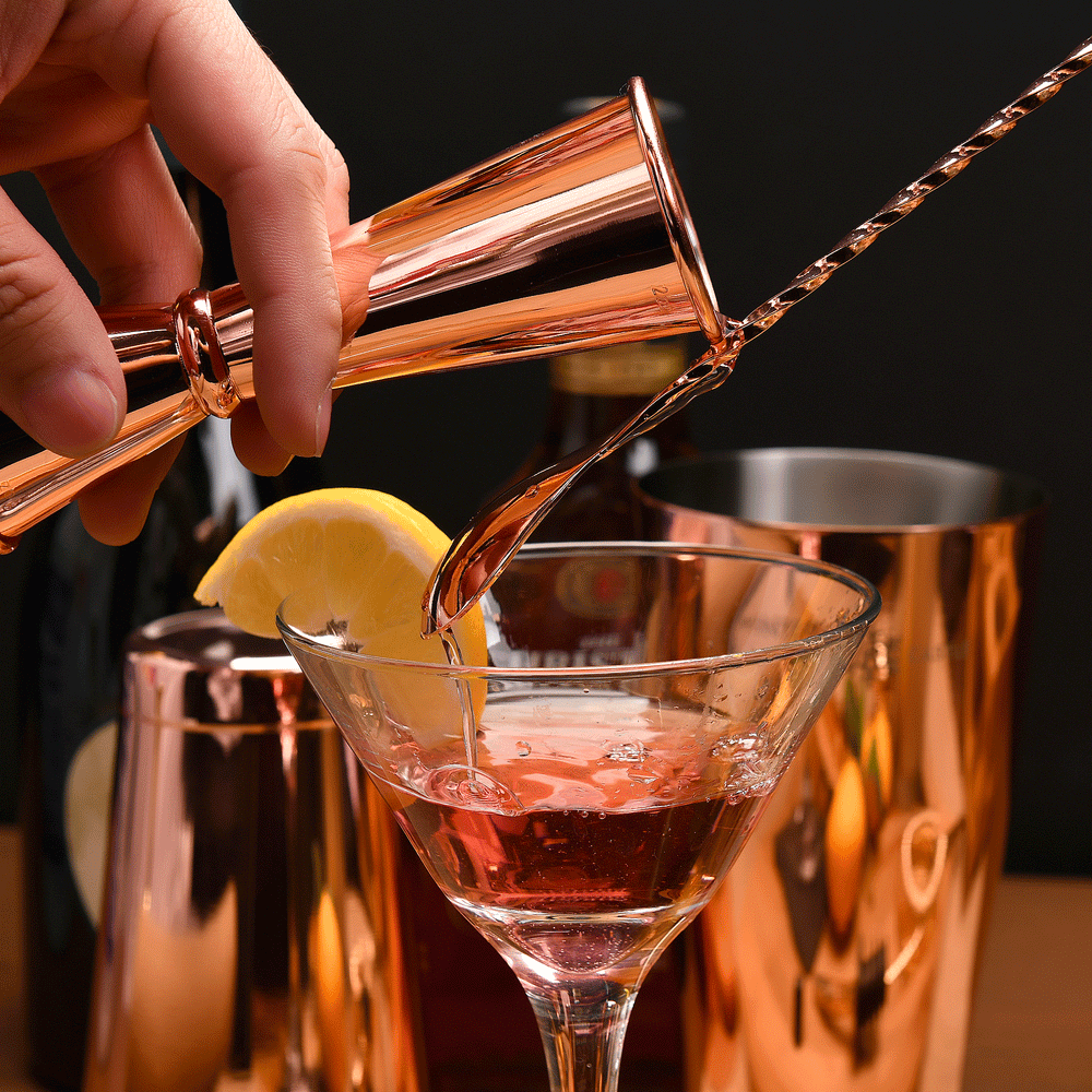 Copper Japanese double jigger pouring over bar spoon into martini glass